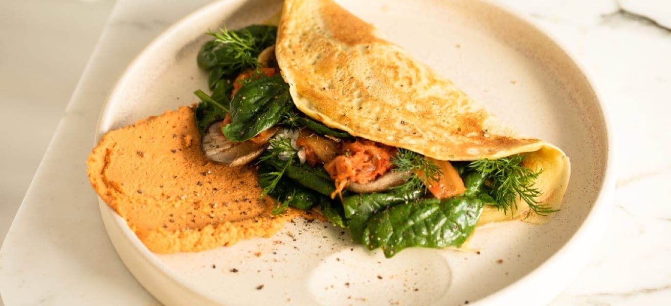 Omelette pliée garnie de légumes frais, servie avec une purée orangée dans une assiette en céramique